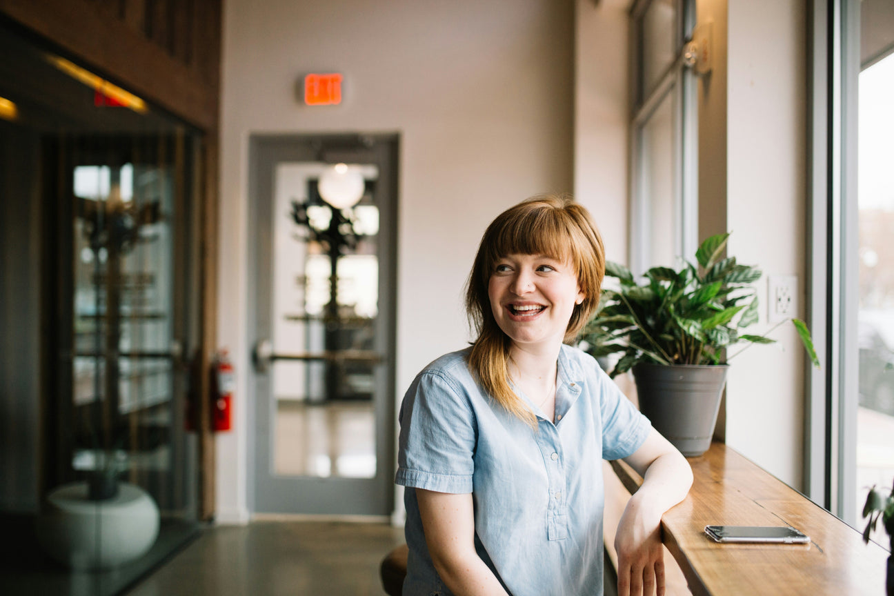 A smiling woman stands in an office space near the door