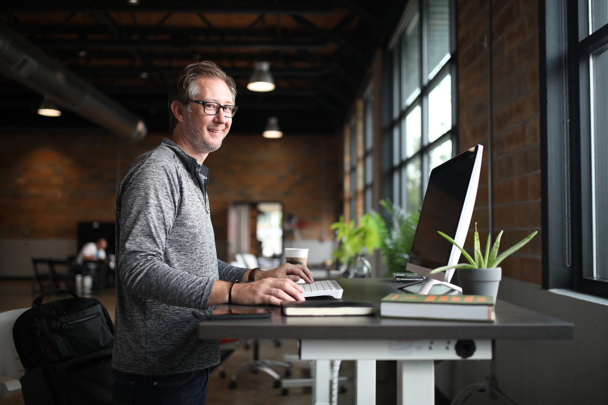 A man walks at a workstation while wondering whether he should get a manual or motorize under desk treadmill