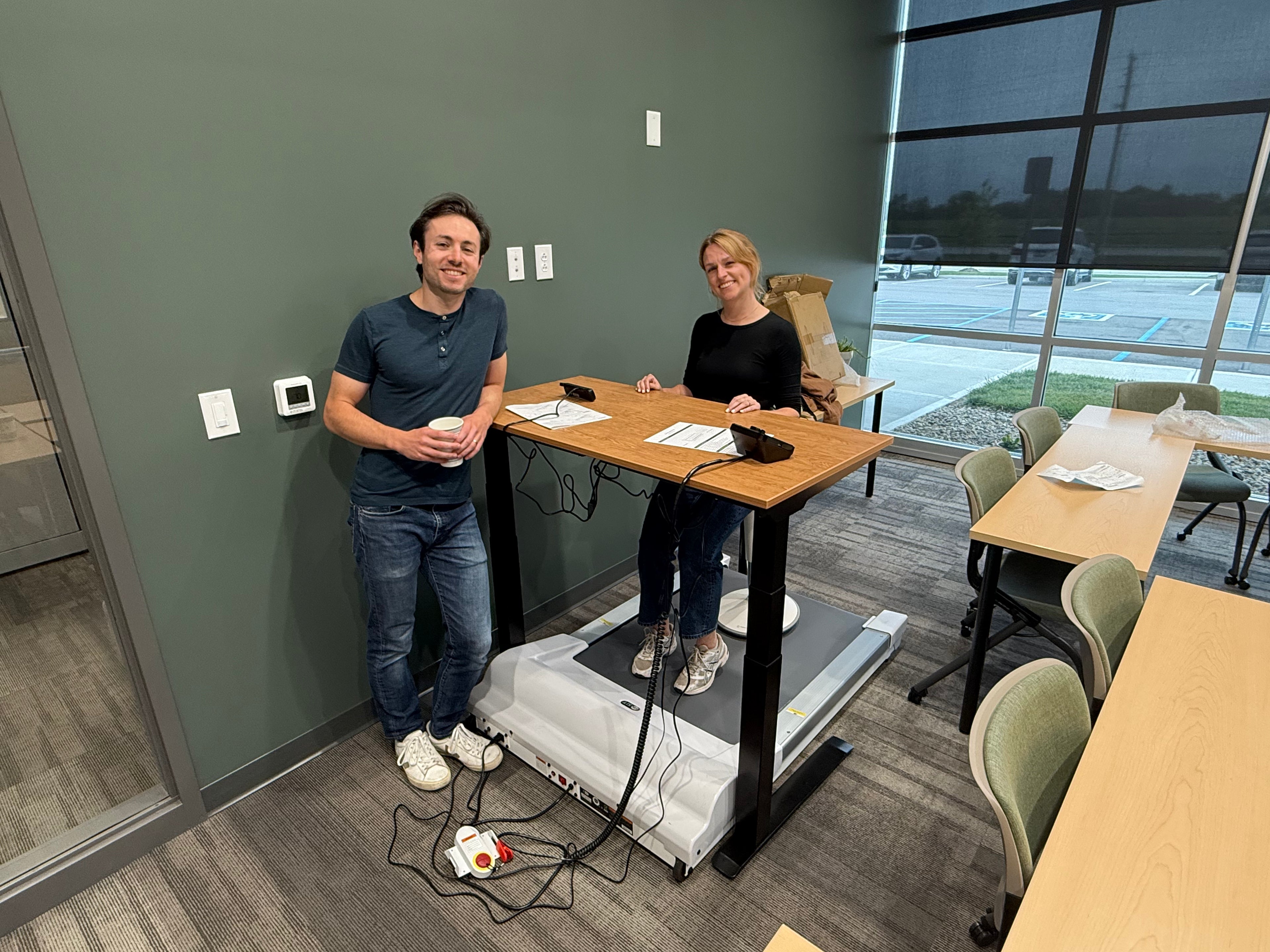 Two people in a room with a treadmill and various equipment.